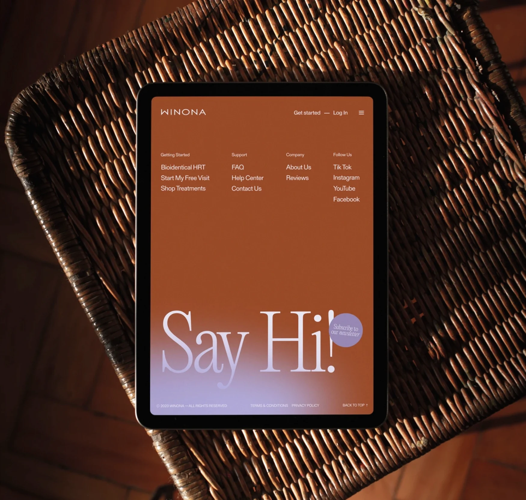 Winona website displayed on a tablet in a woven chair.