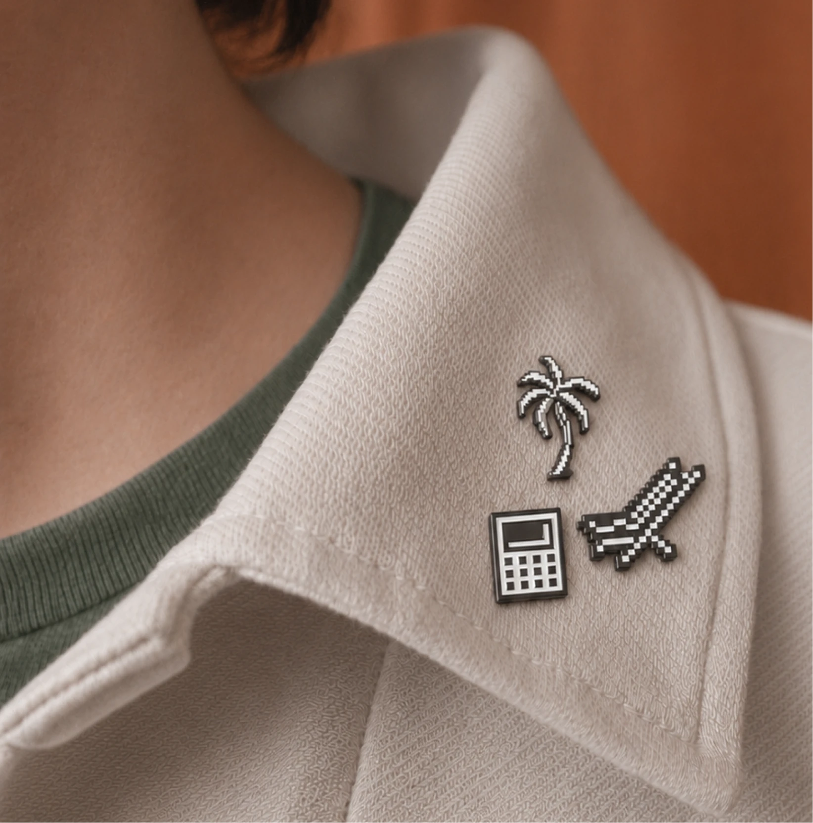 Pixel-art palm tree, calculator and airplane pins on a shirt collar.
