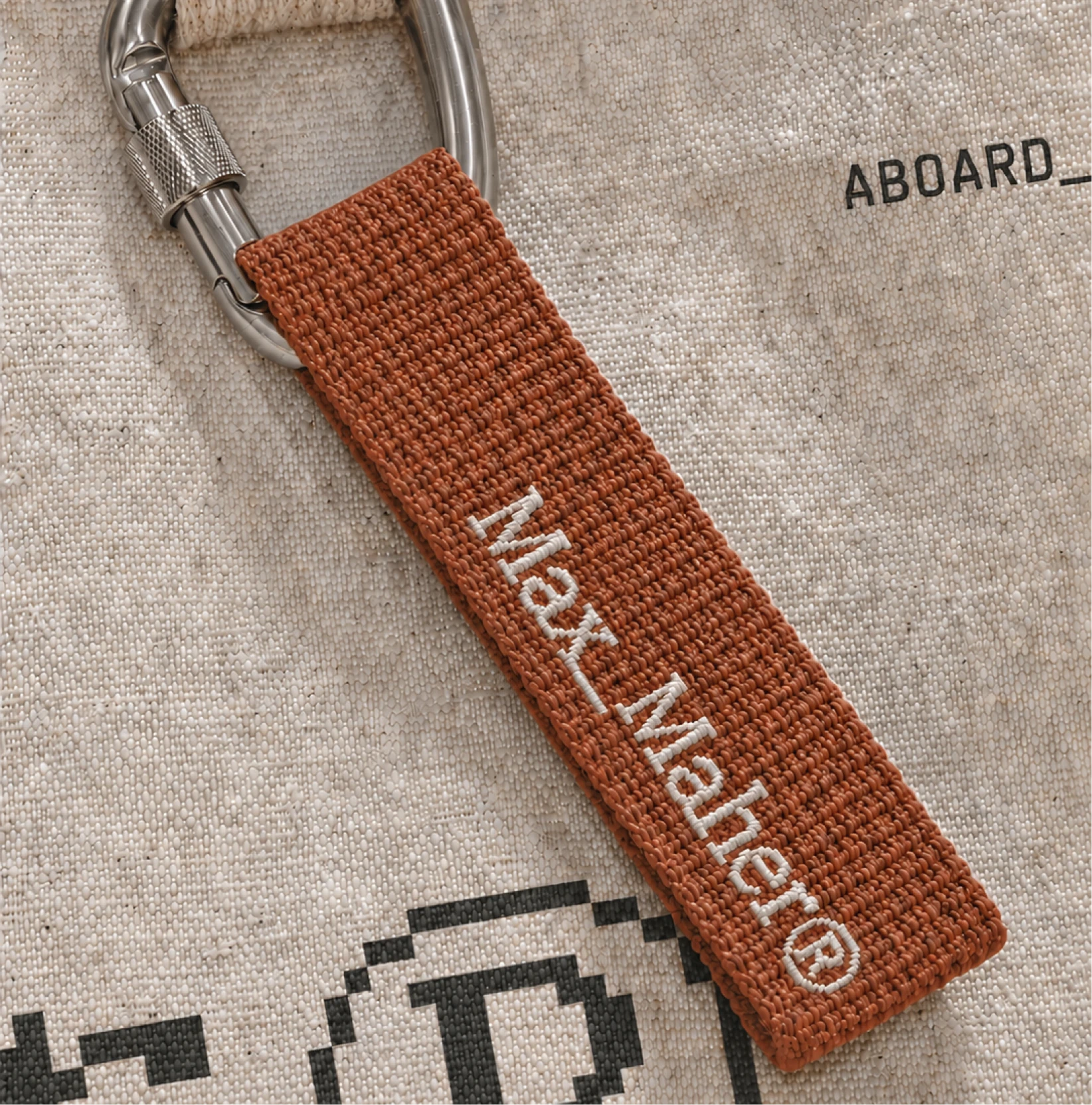 Embroidered orange Max Maher keychain on a canvas bag.