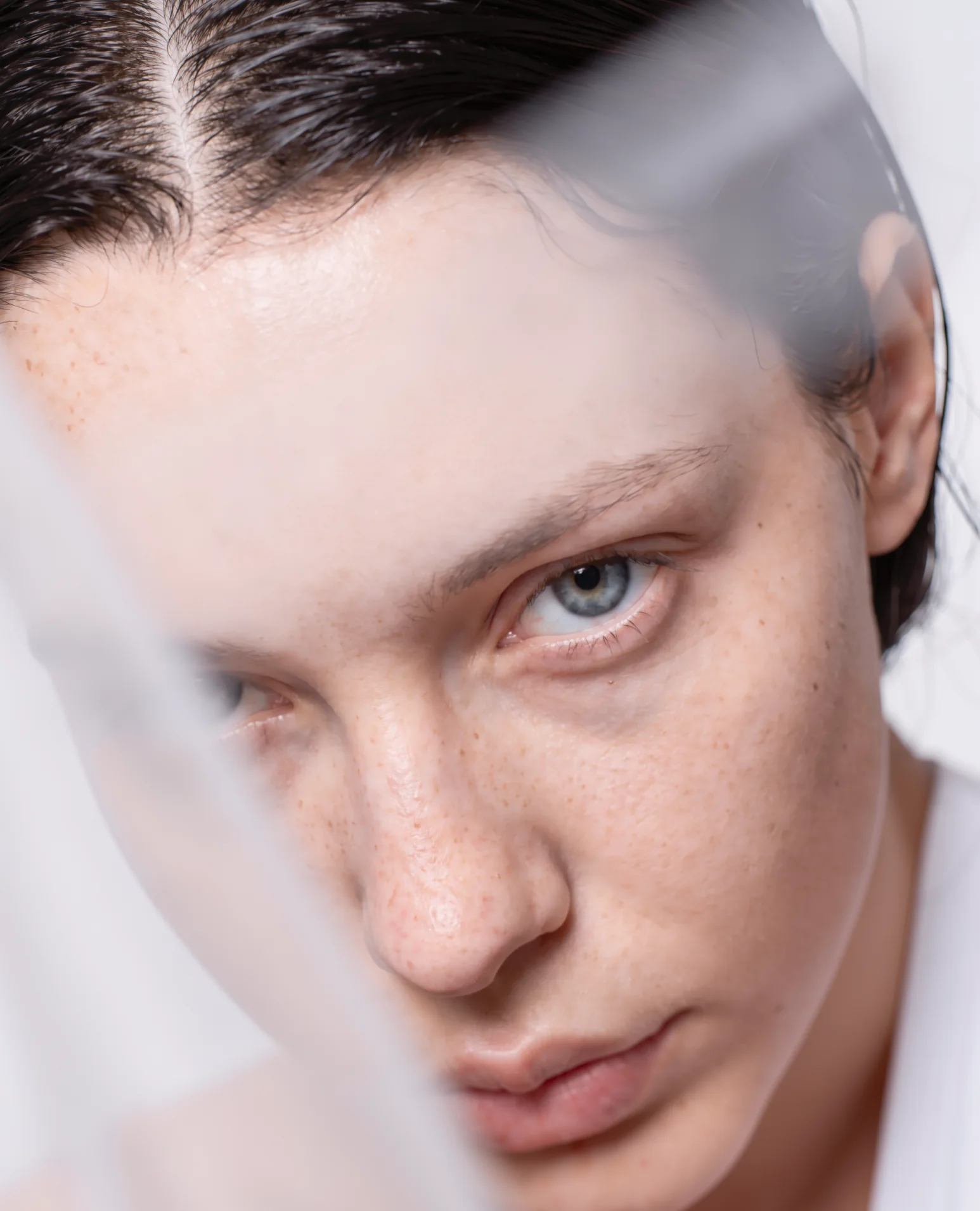 Freckled face partly veiled by a translucent sheet.