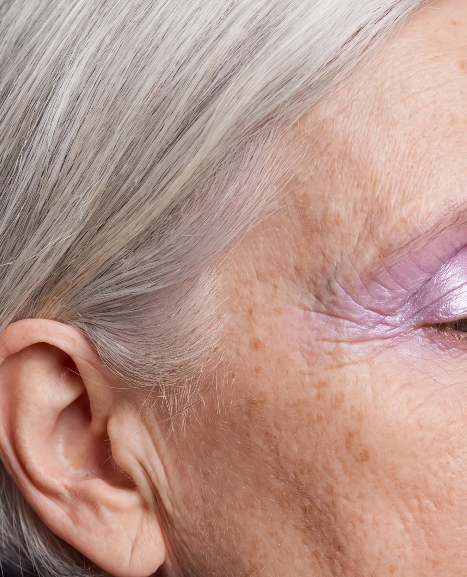 Grey hair, an ear and lilac eyeshadow on older skin.