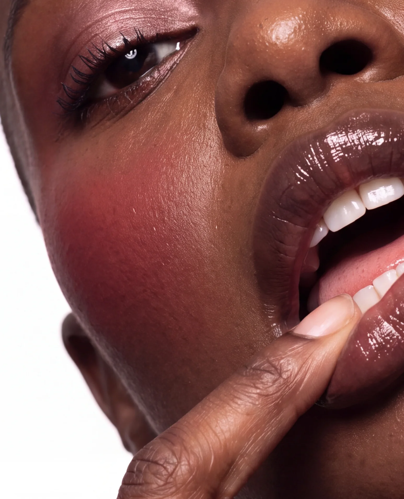 A finger pulling at glossy lips under bold blush.