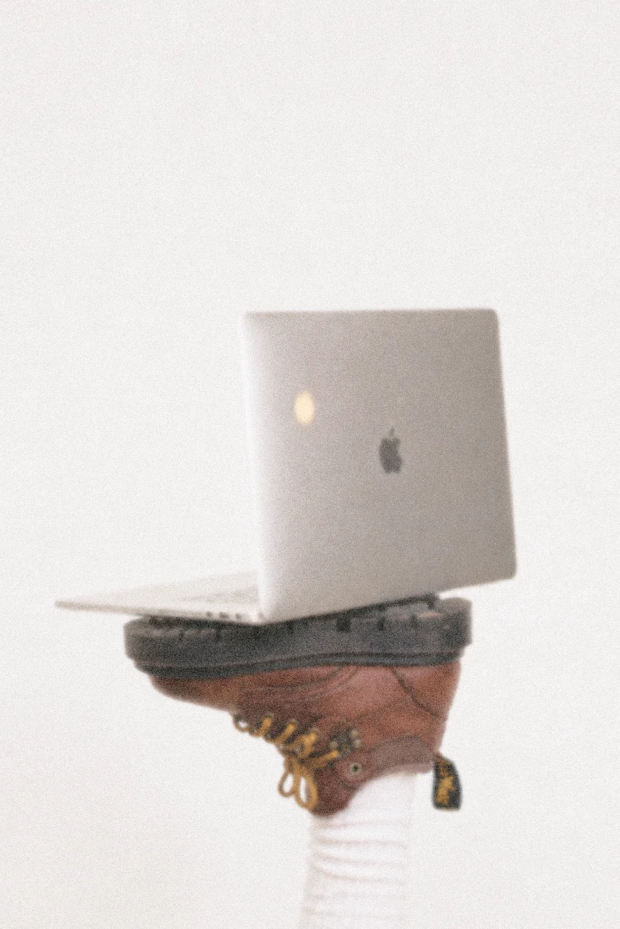 An open laptop balanced on a pair of boots.