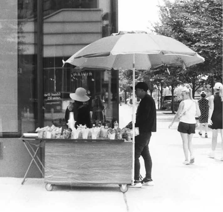 A black-and-white street vendor beneath an umbrella.