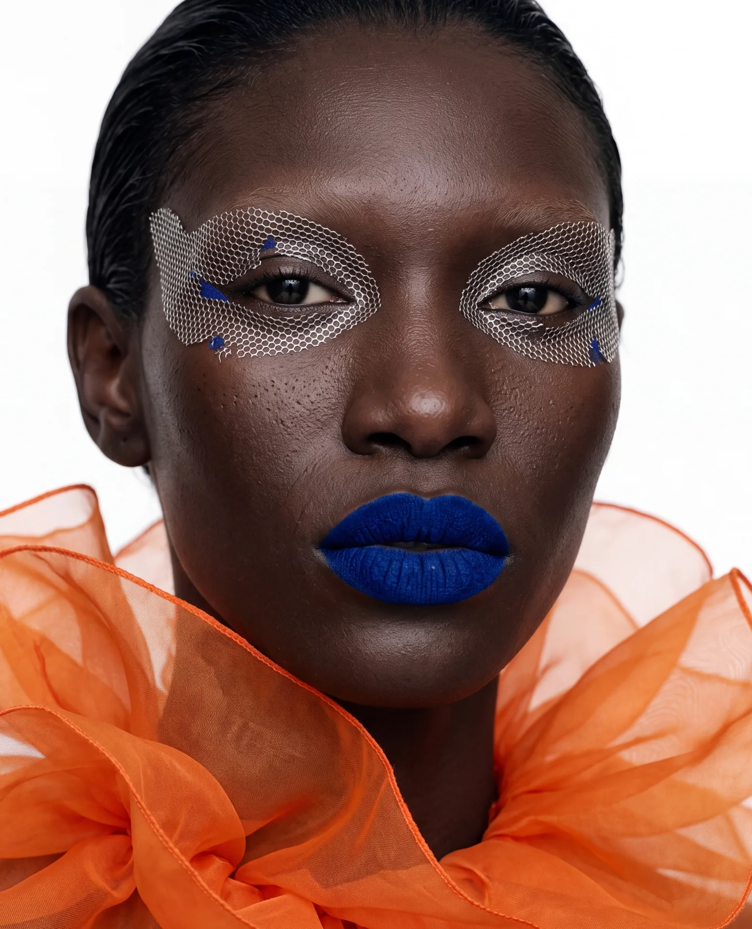 Mesh over both eyes, cobalt-blue lips and a frill of orange tulle.