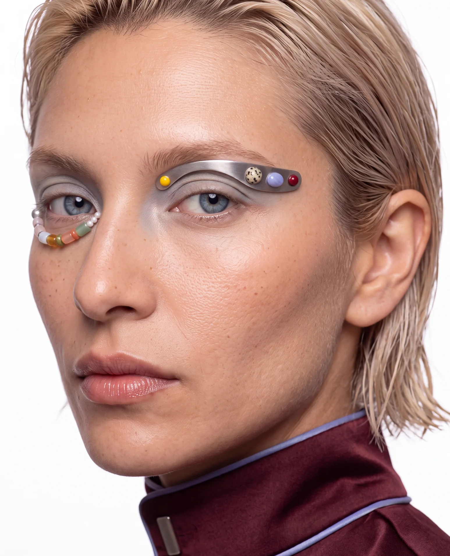Blonde face with a silver brow piece set with coloured beads and a beaded line under the other eye.