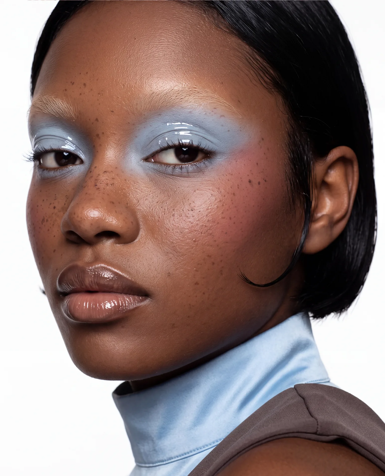 Pale blue lids and glossy nude lips over a baby-blue satin collar.