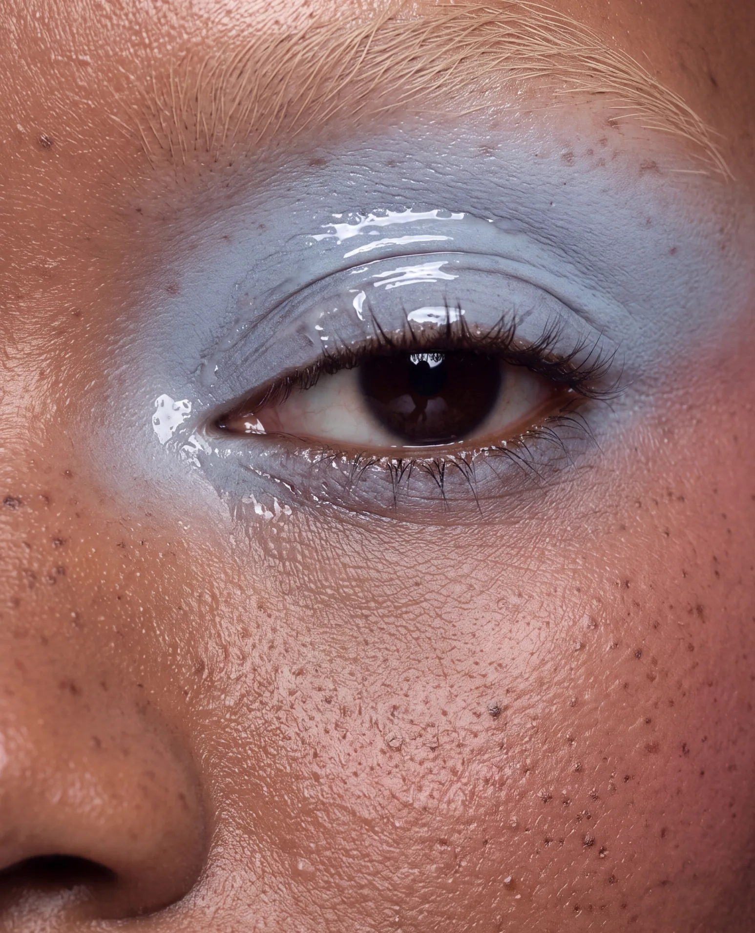 Close-up of a glossy, pale blue lid on deep brown skin.