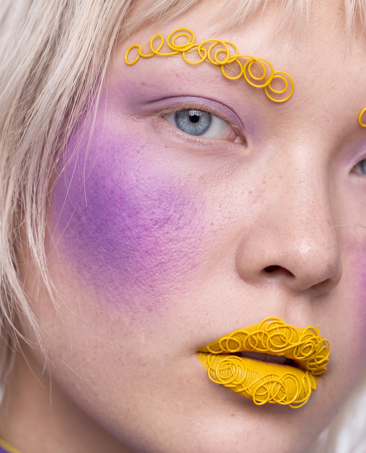 The same face nearer: coiled yellow brows and lips, violet on the cheek.