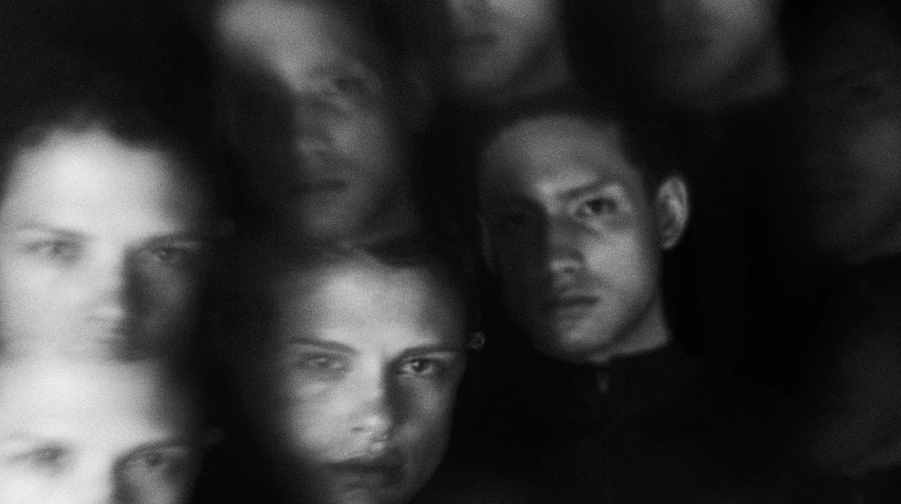 Faces layered and blurred in the dark, a man looking straight ahead among them.