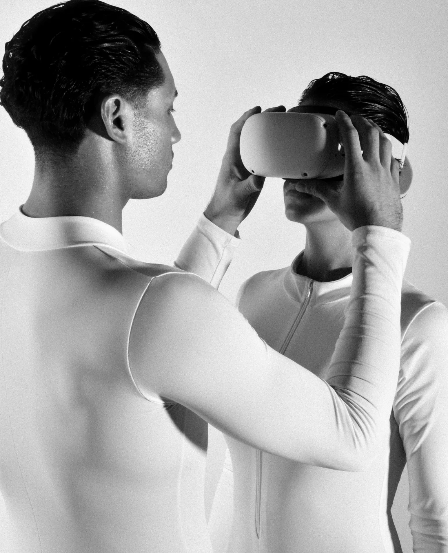 A man fitting a white VR headset on a woman, both in white suits.