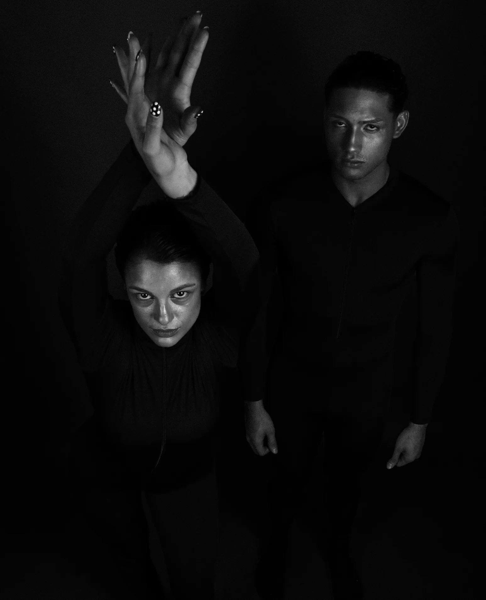 A woman crouching in the dark with an arm raised, a man standing behind her.