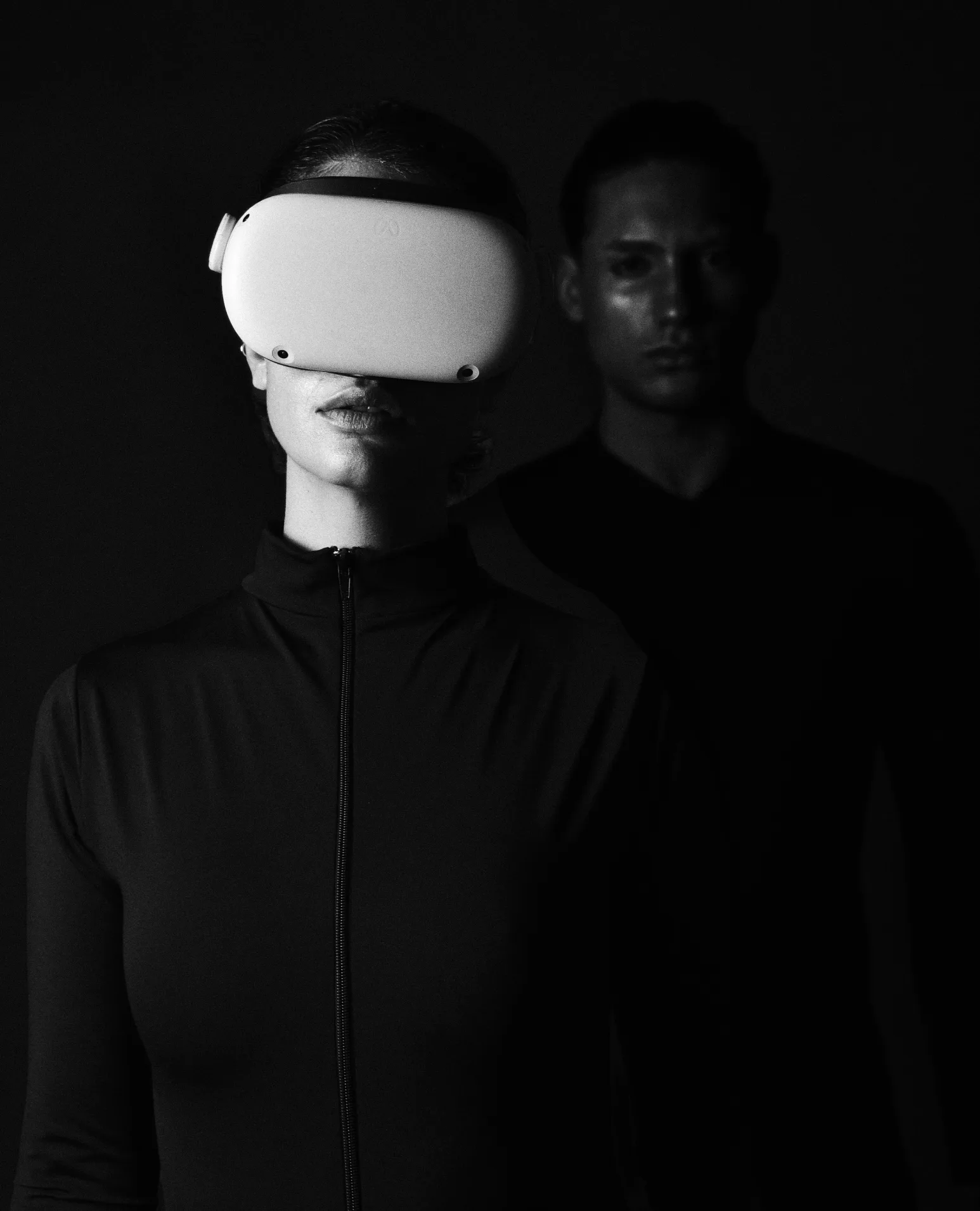 A woman in a white VR headset in the dark, a man behind her.