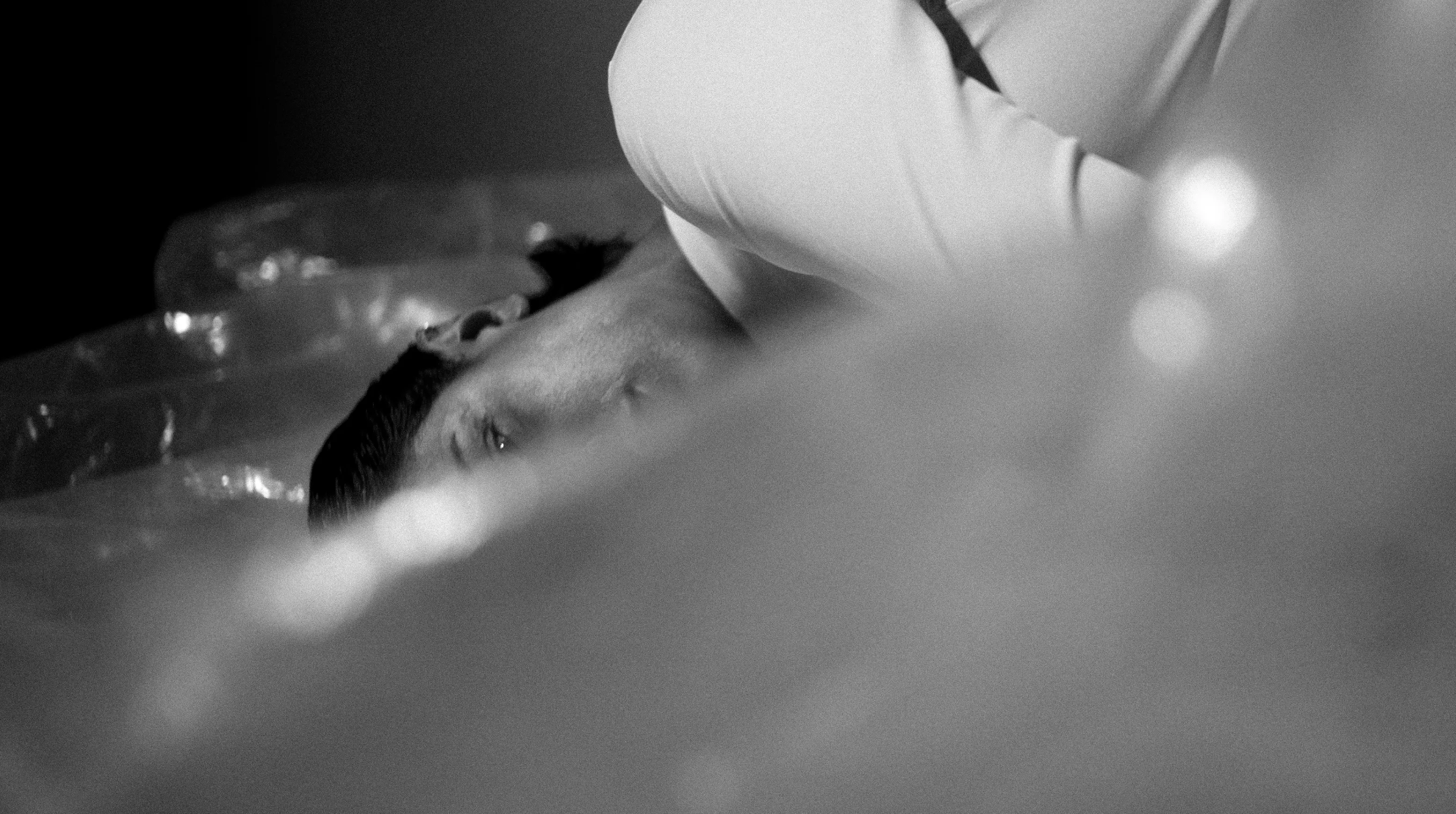 A man lying wrapped in clear plastic, a figure in white bending over him.